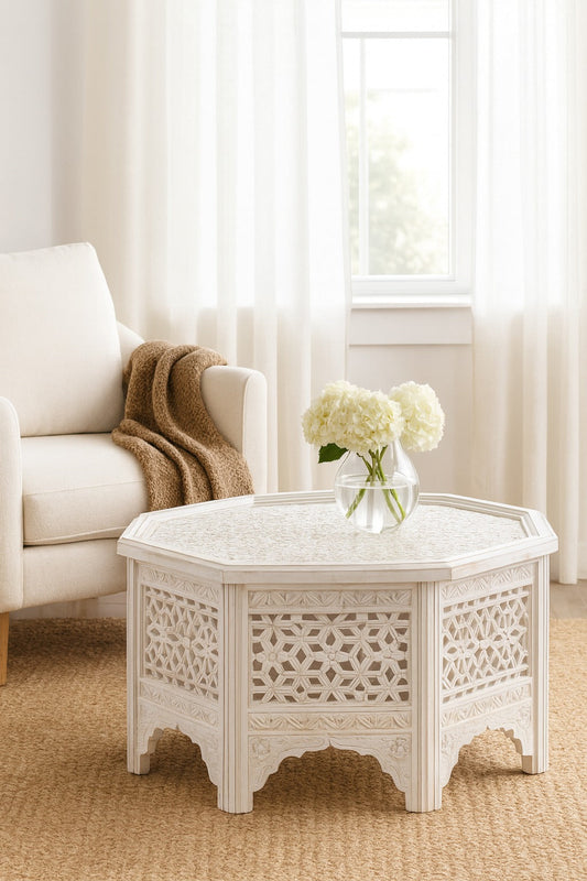 White ornate coffee table with a vase of flowers in a living room setting.