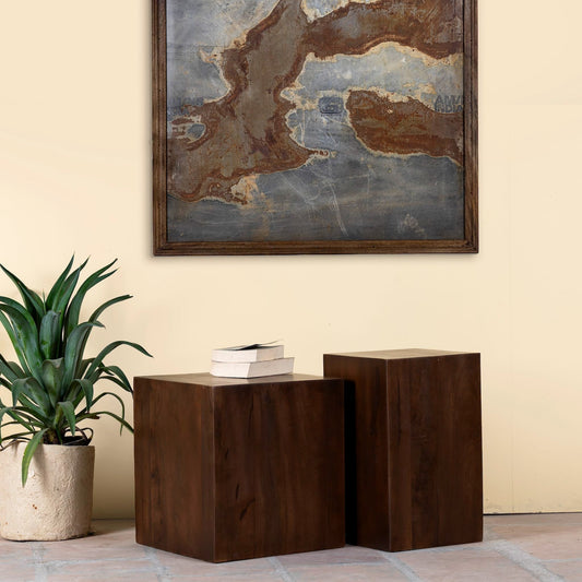 Wooden side tables with a plant and books in a room with a large framed abstract painting on the wall.