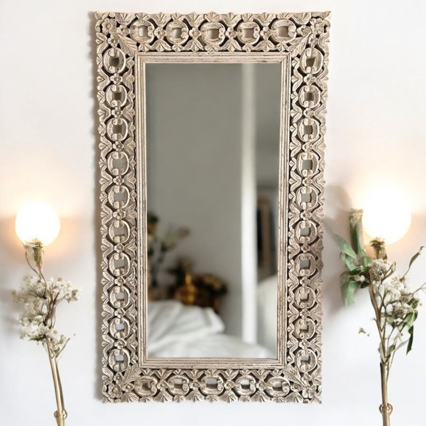 A large, rectangular, handcarved wooden vanity wall mirror with a floral and geometric latticework frame, displayed on a white wall with a mirrored reflection of a garden in the background.
